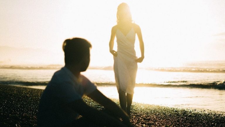 man sitting on sunset beach with woman approaching