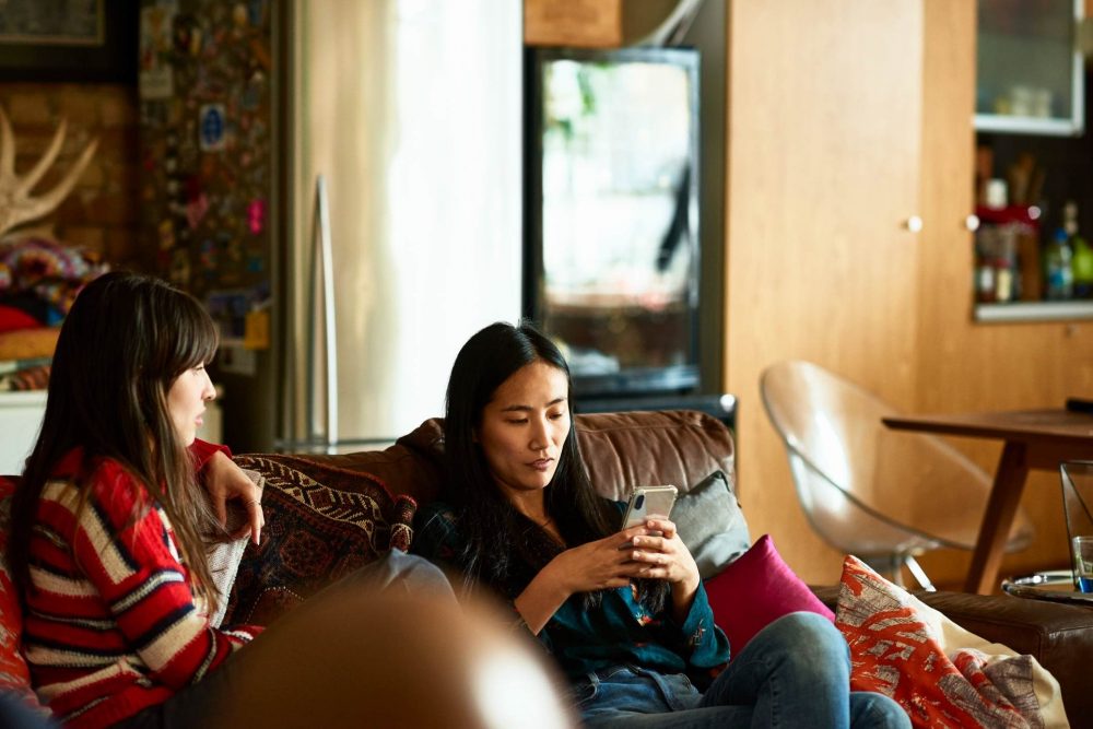 woman-sitting-on-sofa-with-friend-using-cell-phone